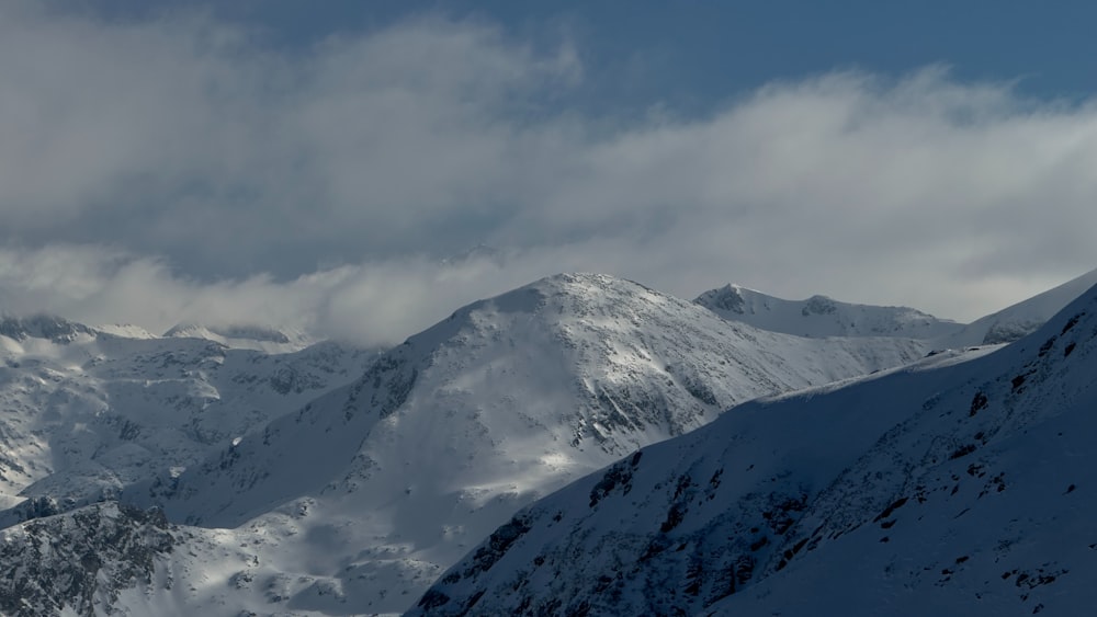 a snow covered mountain range under a cloudy sky