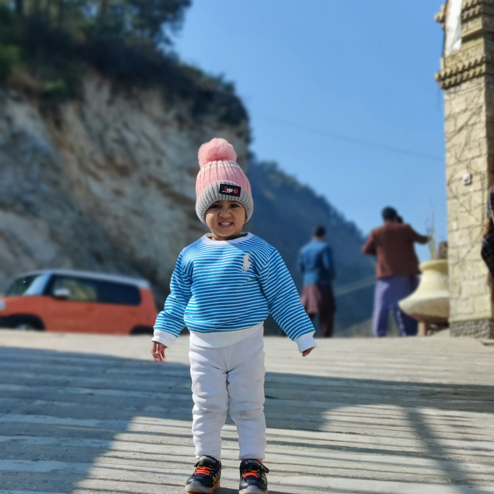 a small child in a blue shirt and a pink hat on a skateboard