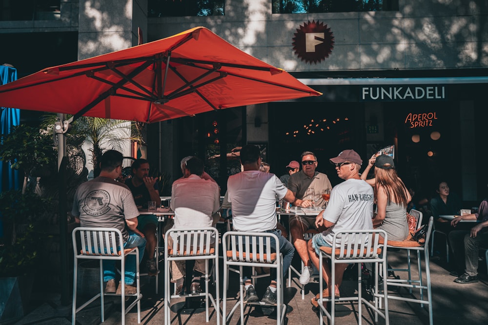 a group of people sitting around a table under an umbrella