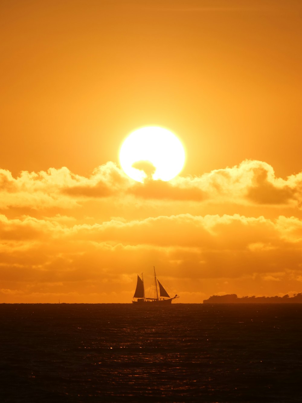 a sailboat in the ocean with the sun in the background