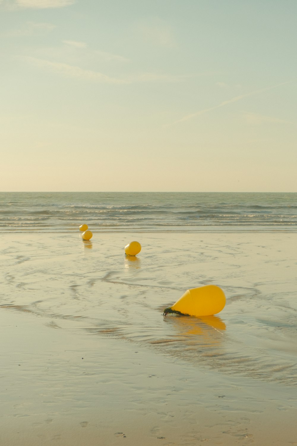 a group of yellow buoys floating on top of a sandy beach