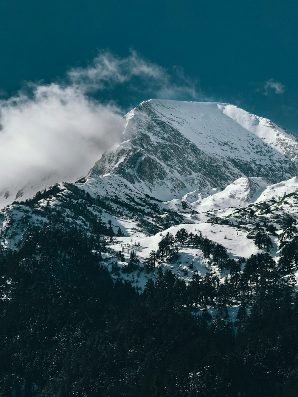 a mountain covered in snow and clouds under a blue sky