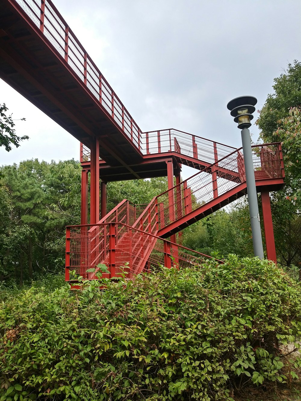 a red metal bridge over a lush green forest