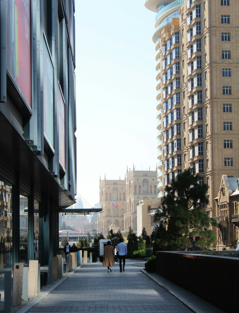 a couple of people walking down a street next to tall buildings