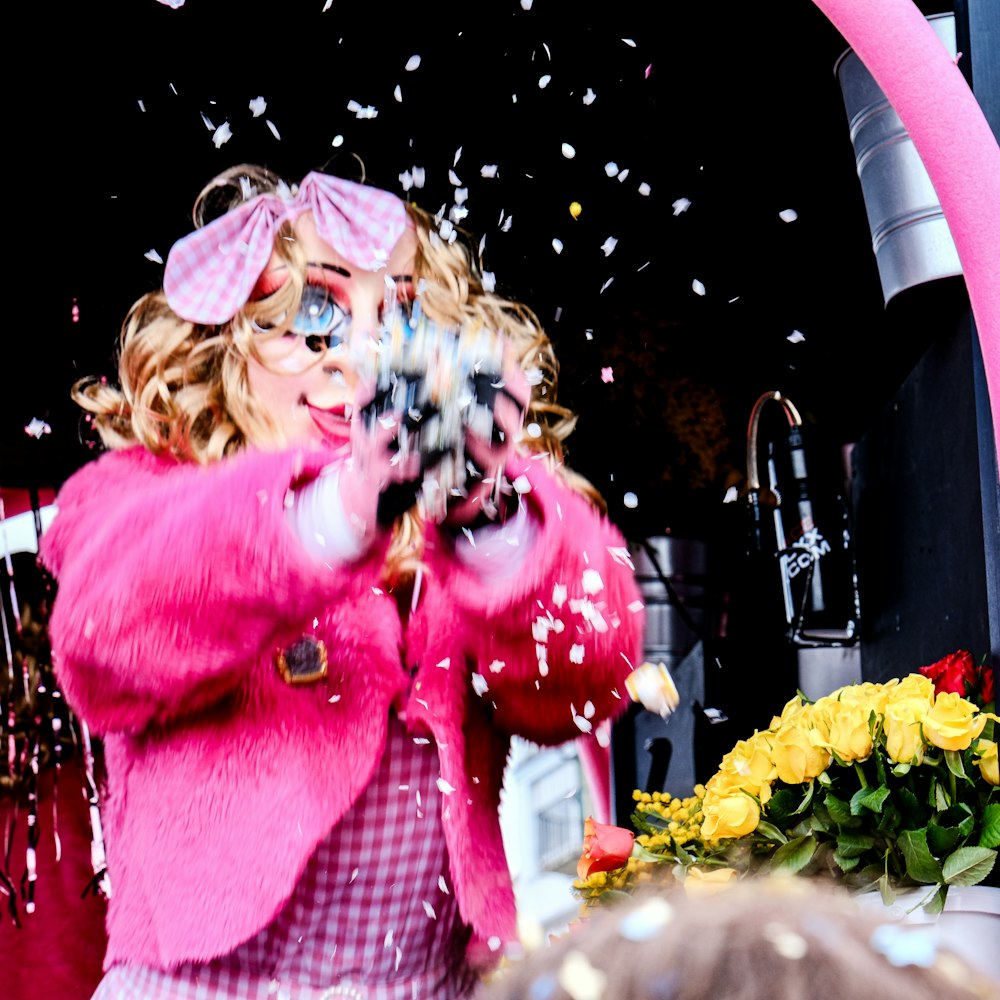 a woman in a pink coat throwing confetti on her face