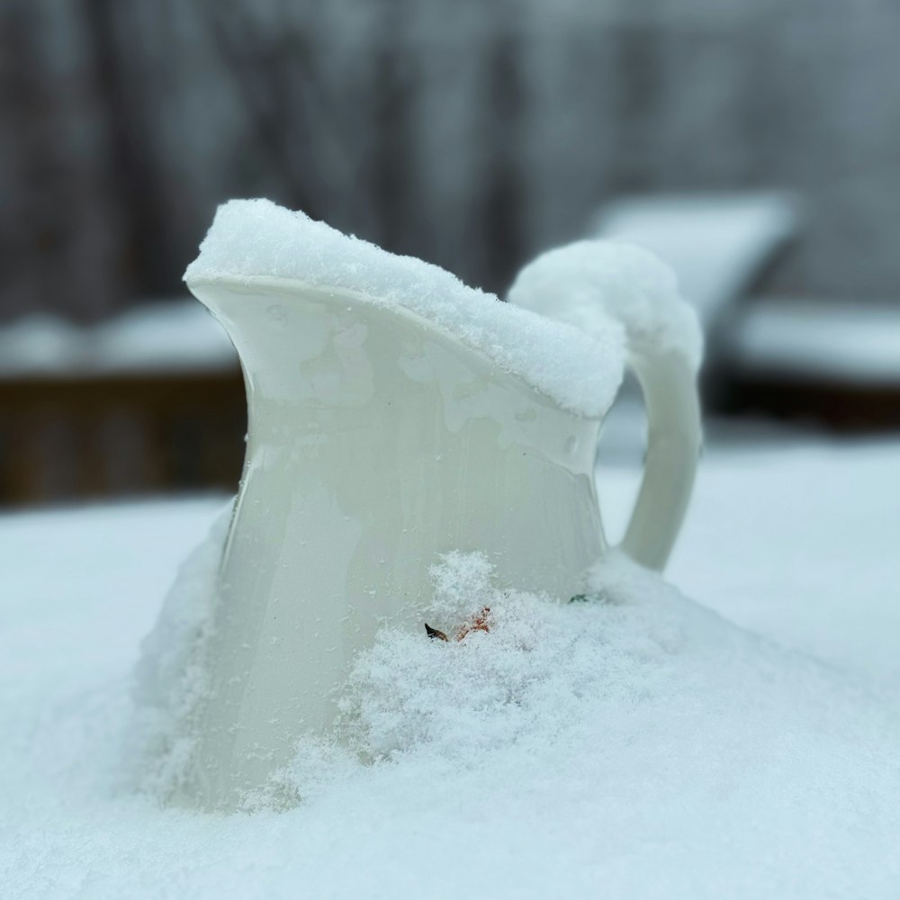 a snow covered pitcher sitting on top of a pile of snow