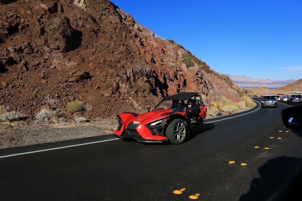 a red car driving down a road next to a mountain