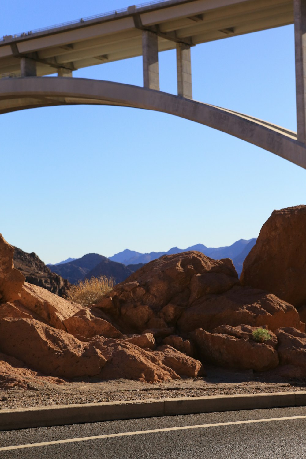 a road under a bridge with a mountain range in the background