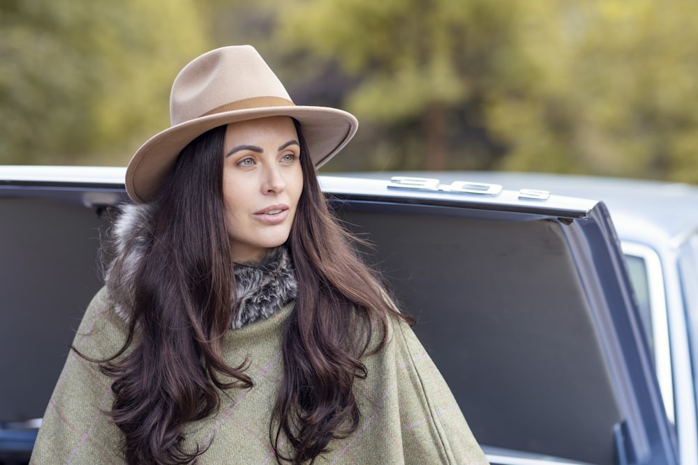 a woman wearing a hat and a cape standing next to a car