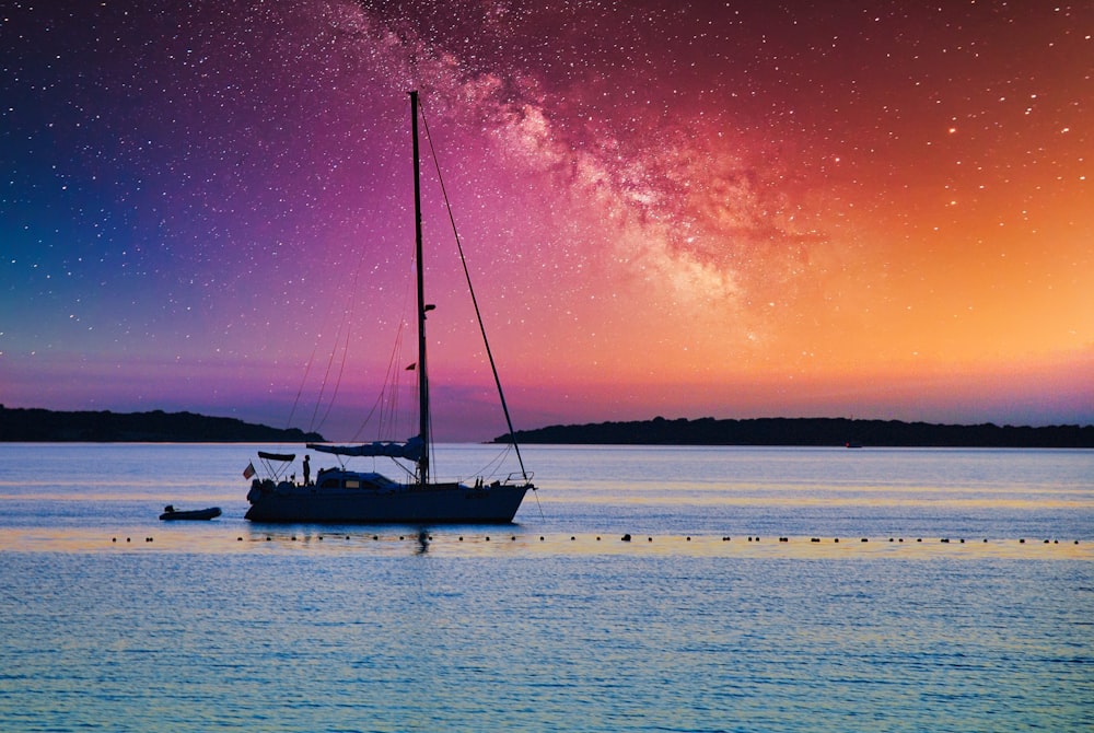 a sailboat floating in the water under a night sky filled with stars