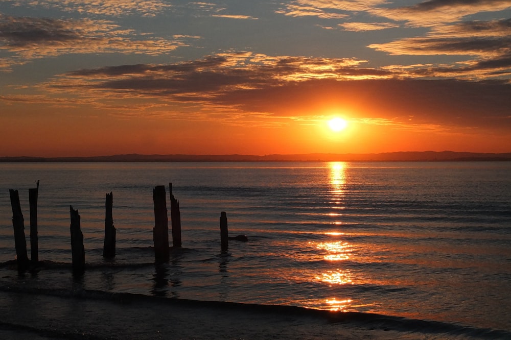 the sun is setting over the ocean with a pier in the foreground