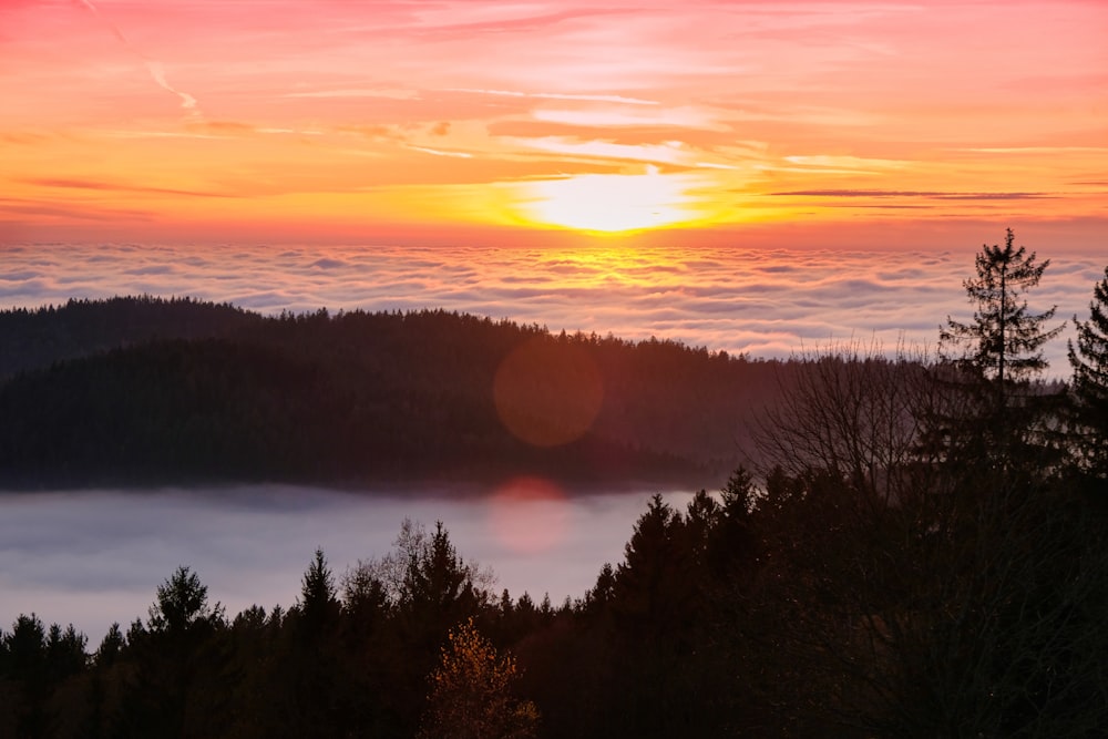 the sun is setting over the clouds in the mountains