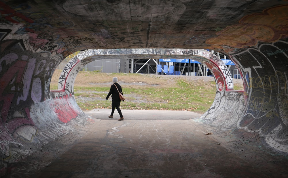 a person walking through a tunnel covered in graffiti