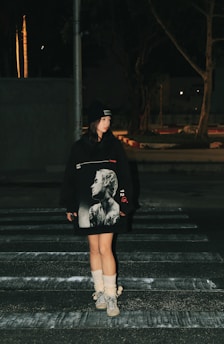 a woman walking across a cross walk at night