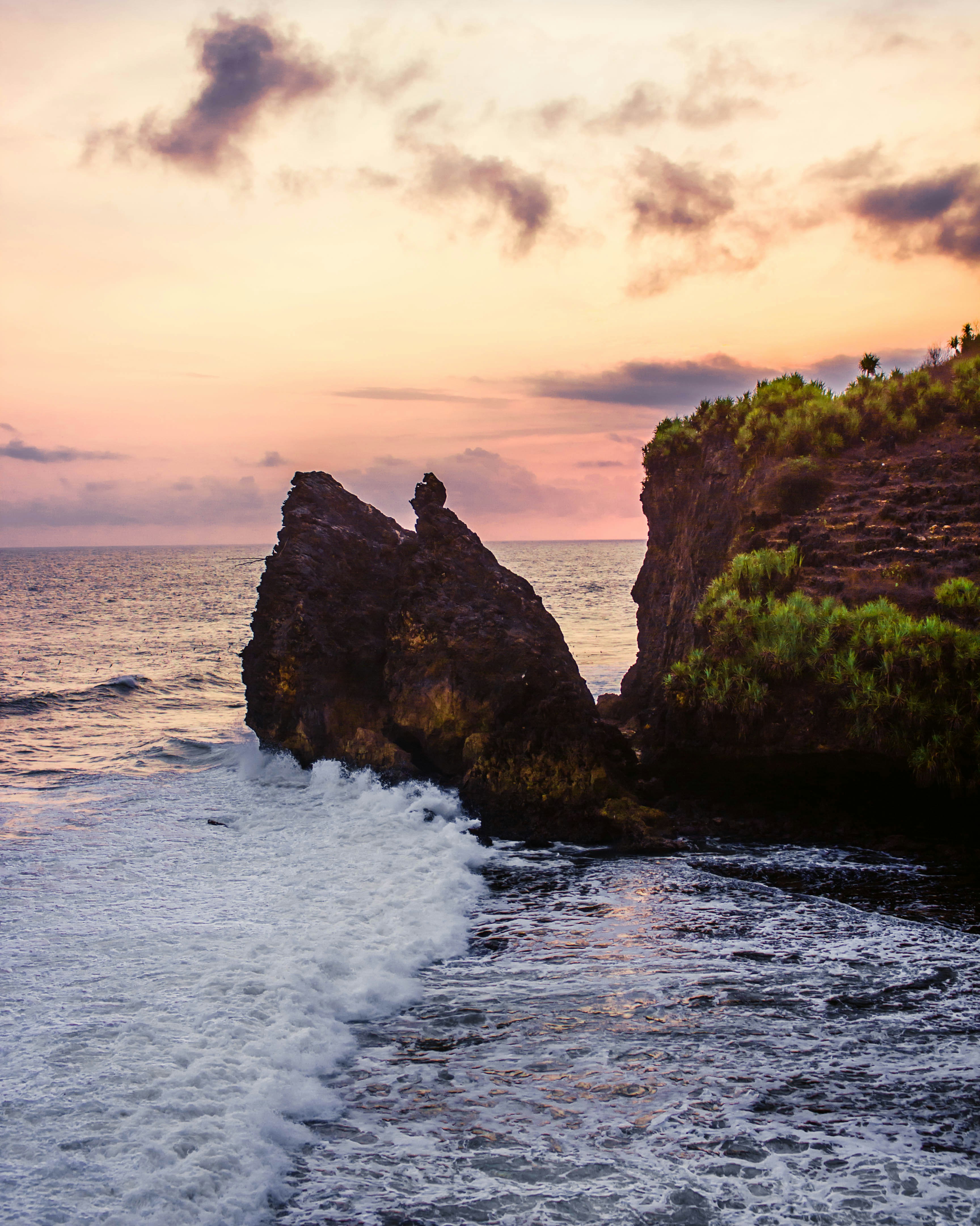 Una persona sentada en la cima de una roca cerca del océano
