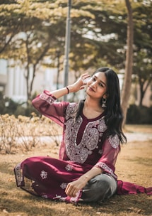 a woman sitting on the ground wearing a maroon dress
