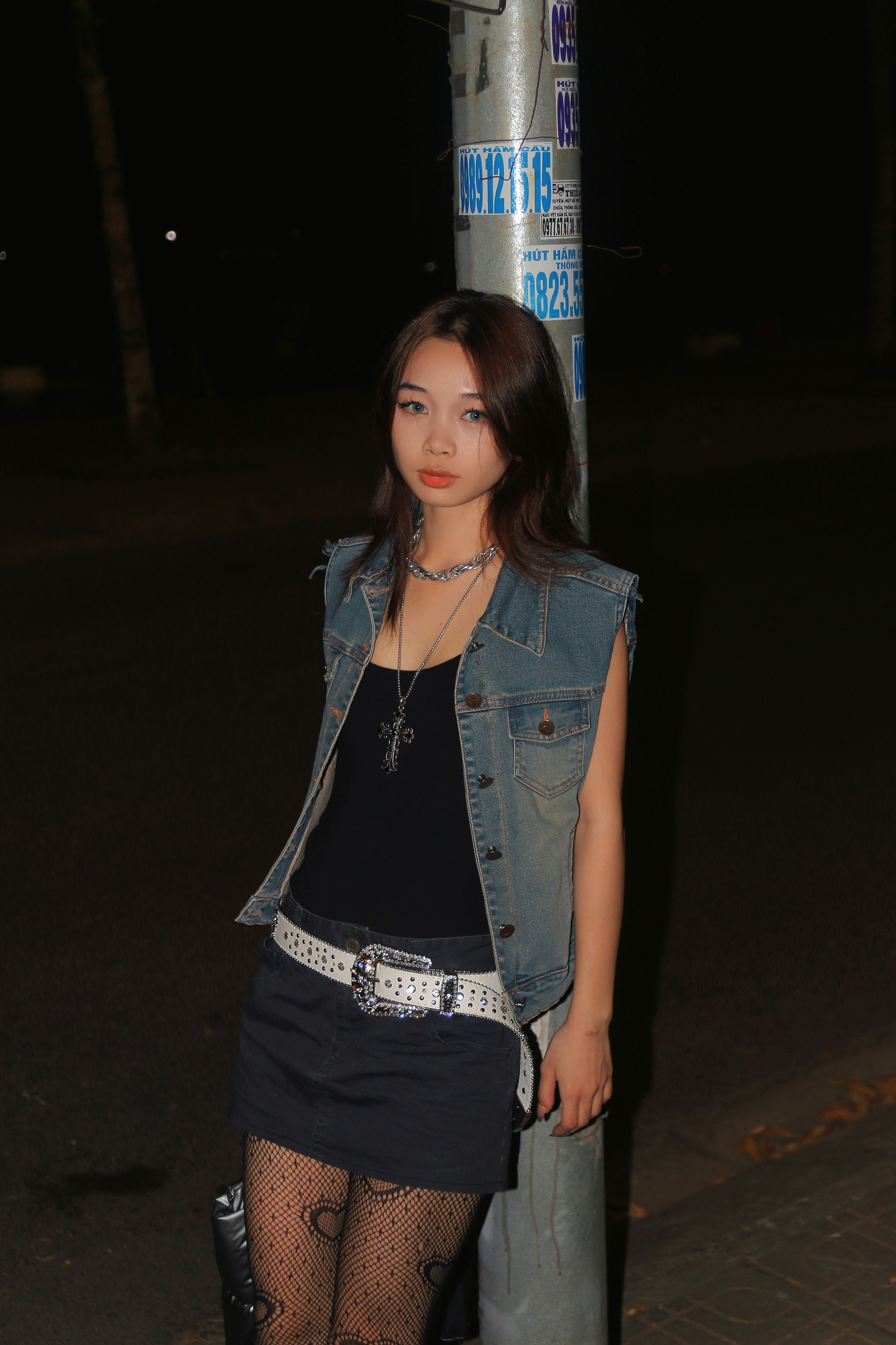 a woman standing next to a pole wearing a jean vest