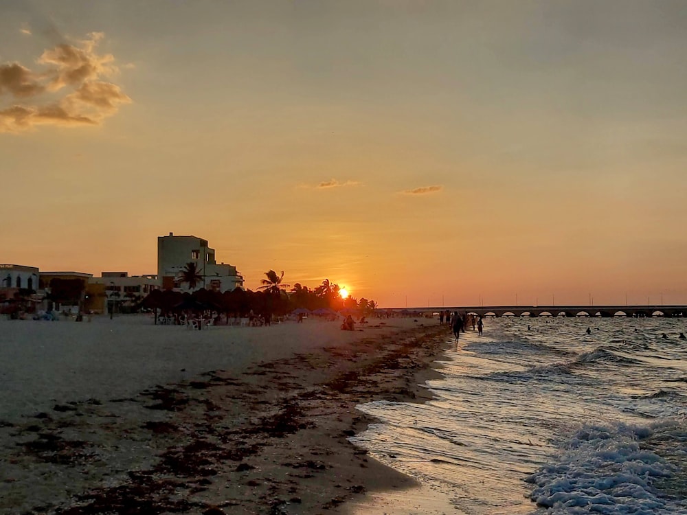 Il sole sta tramontando sulla spiaggia mentre le persone camminano sulla sabbia
