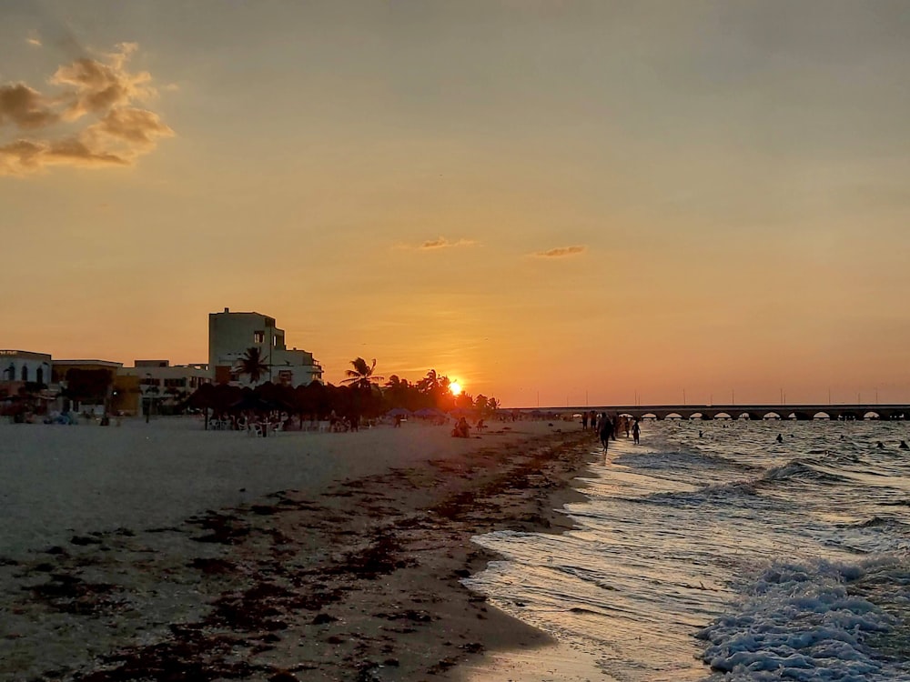 the sun is setting on the beach as people walk on the sand