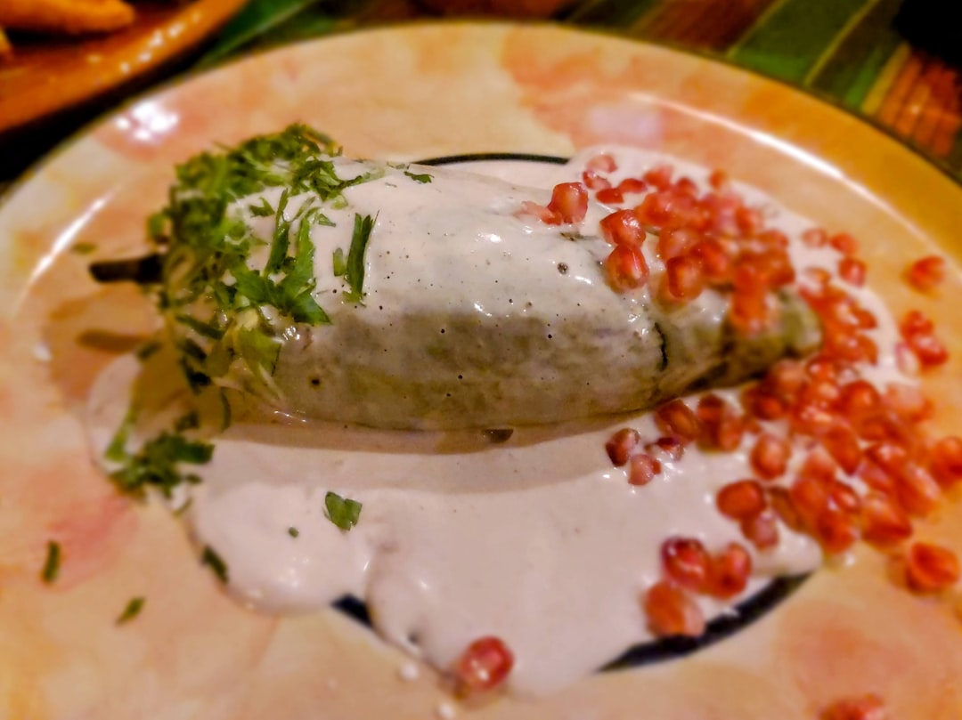 a plate topped with a burrito covered in sauce, Chile en nogada