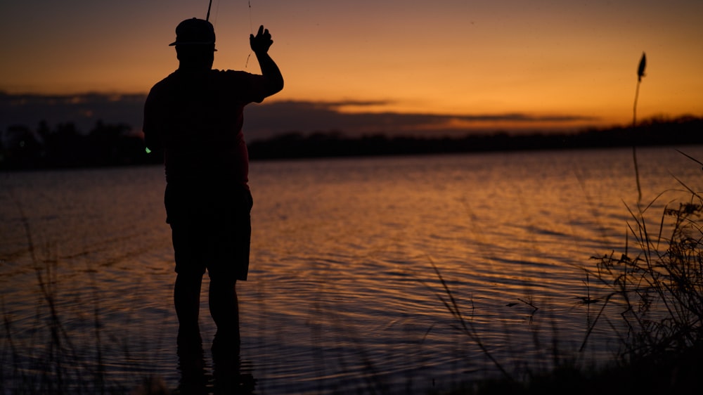 a man standing next to a body of water holding a fishing pole