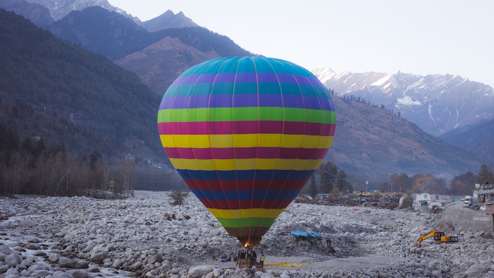 a large colorful hot air balloon flying over a rocky field