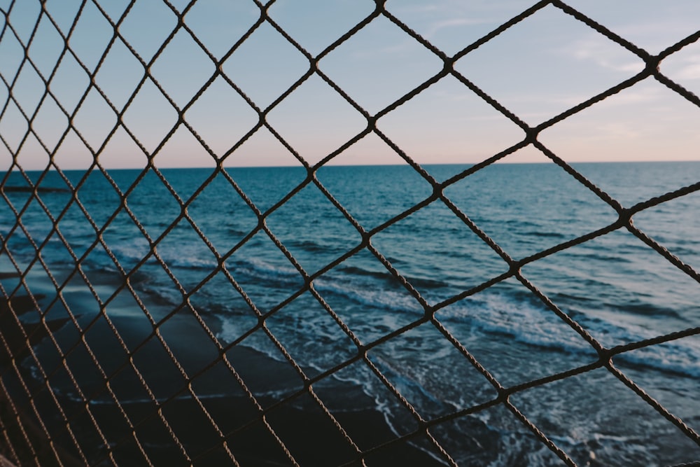 a view of the ocean through a chain link fence