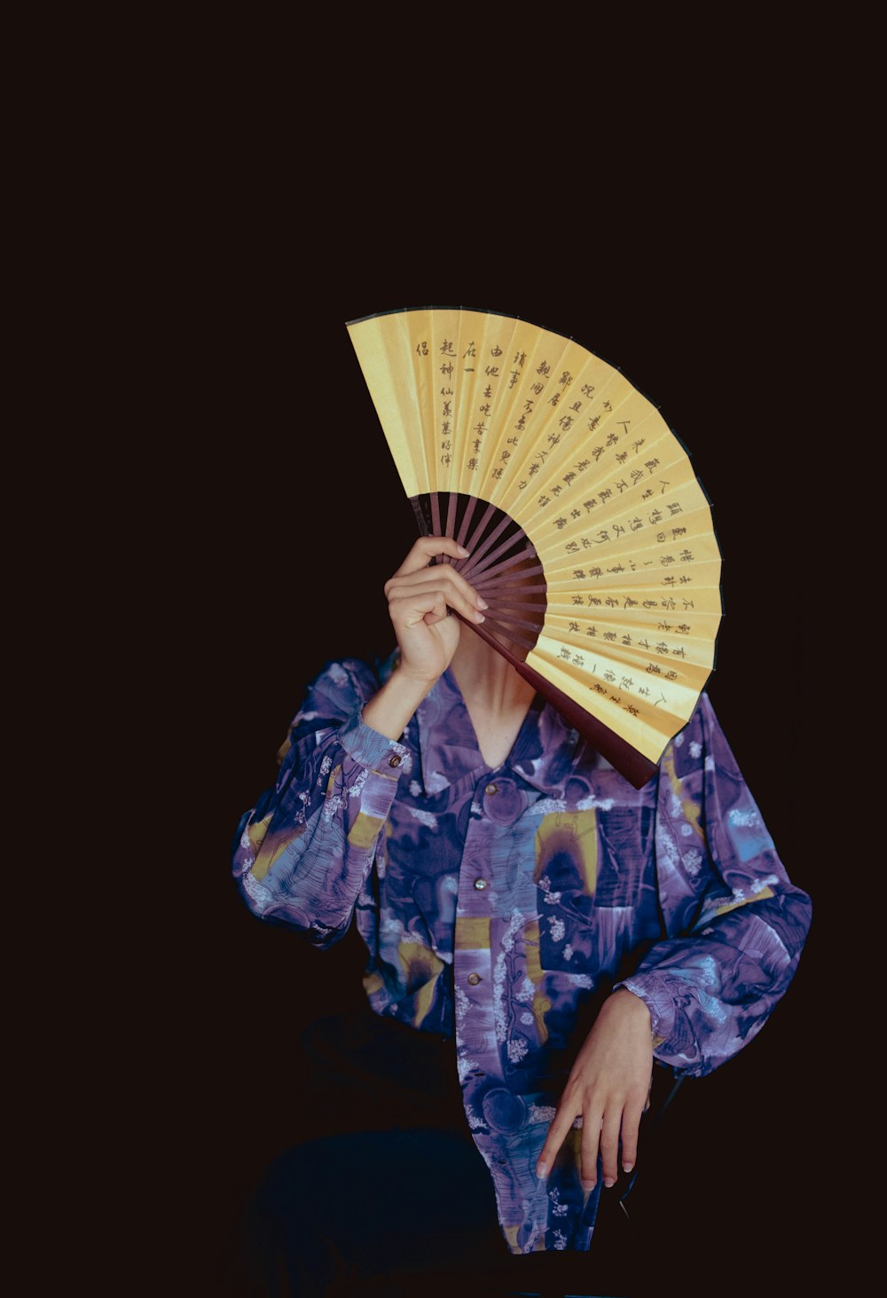 a woman holding a yellow fan over her face