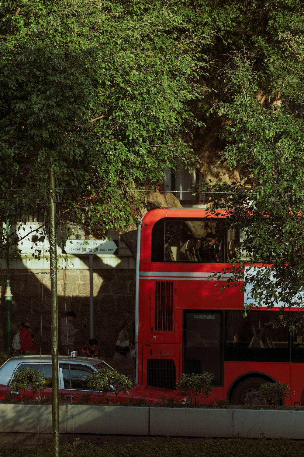 a red double decker bus parked next to a tree