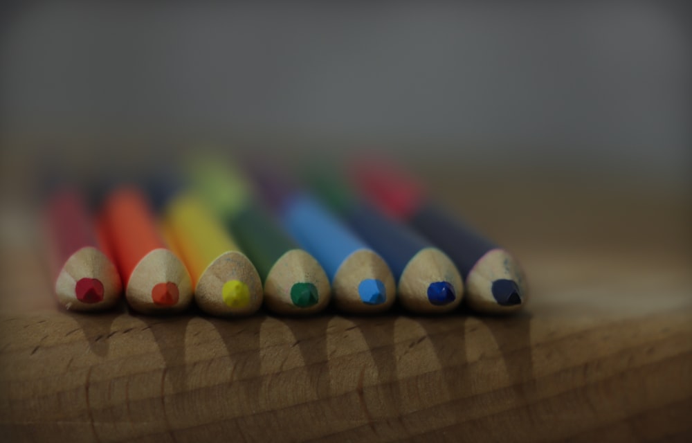 a row of colored pencils sitting on top of a wooden table