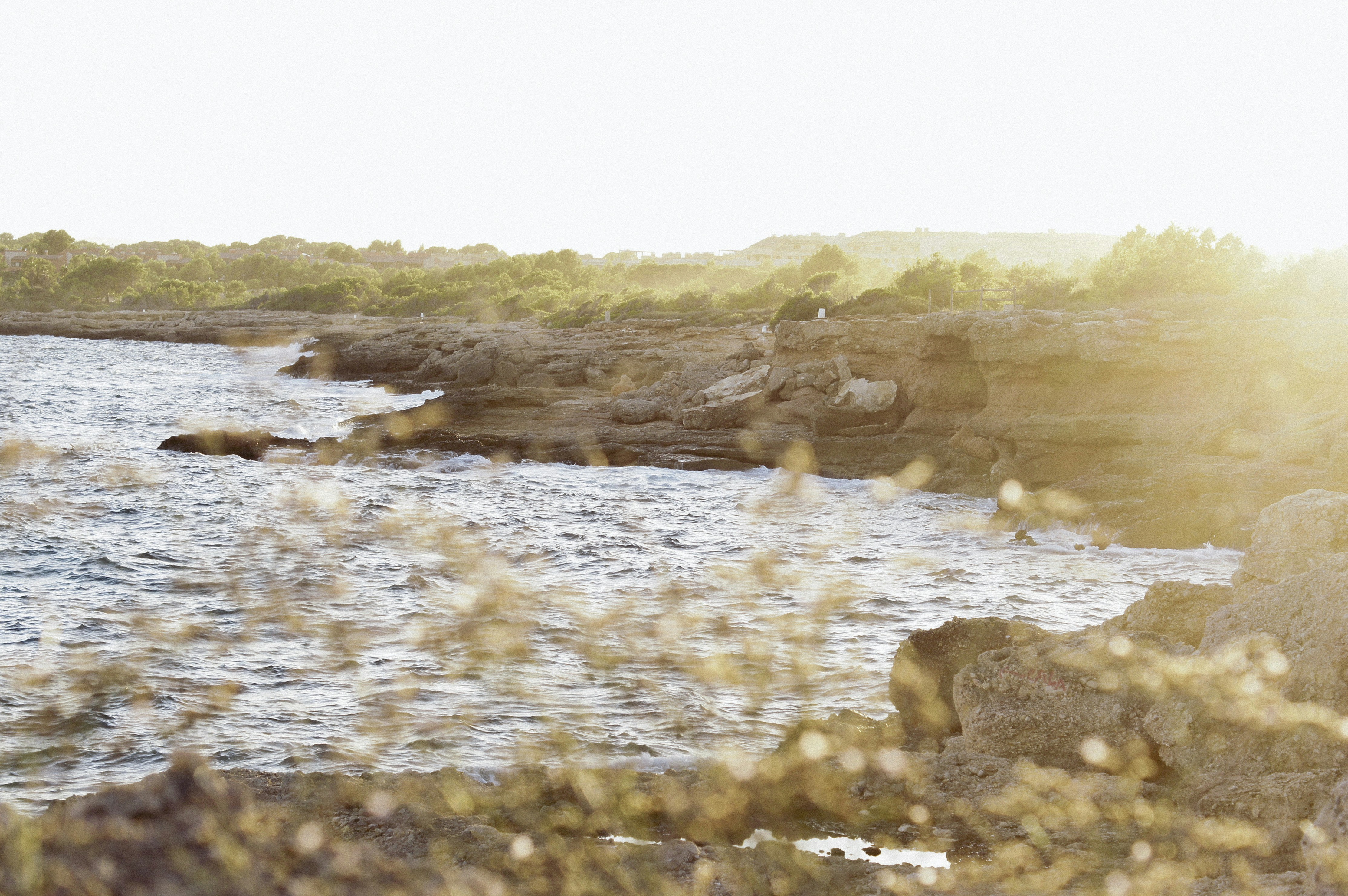 the sun shines on the water and rocks near the shore