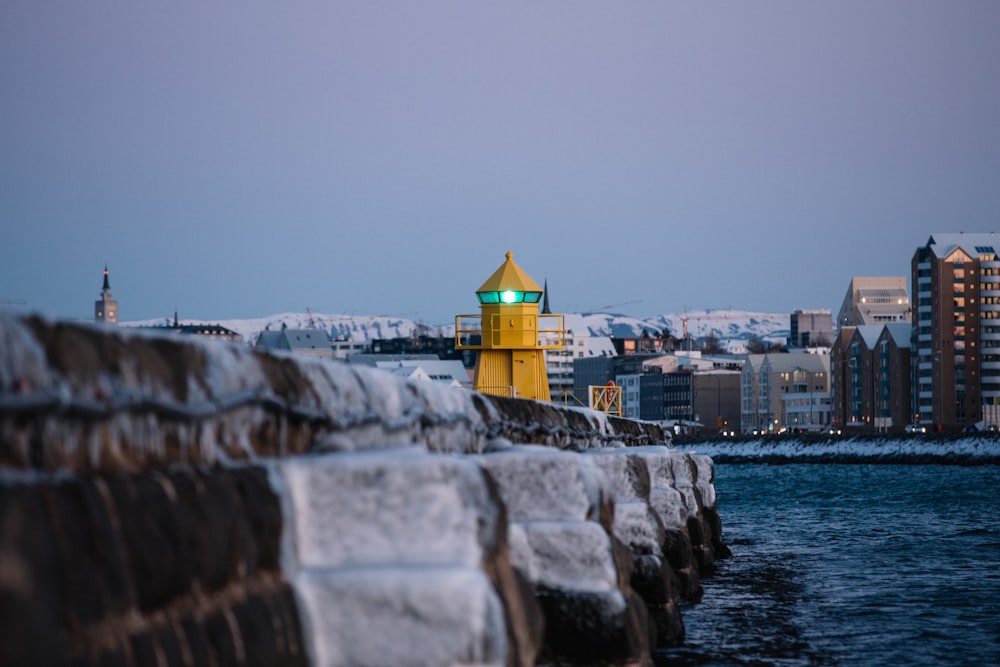 a yellow lighthouse sitting on the side of a body of water