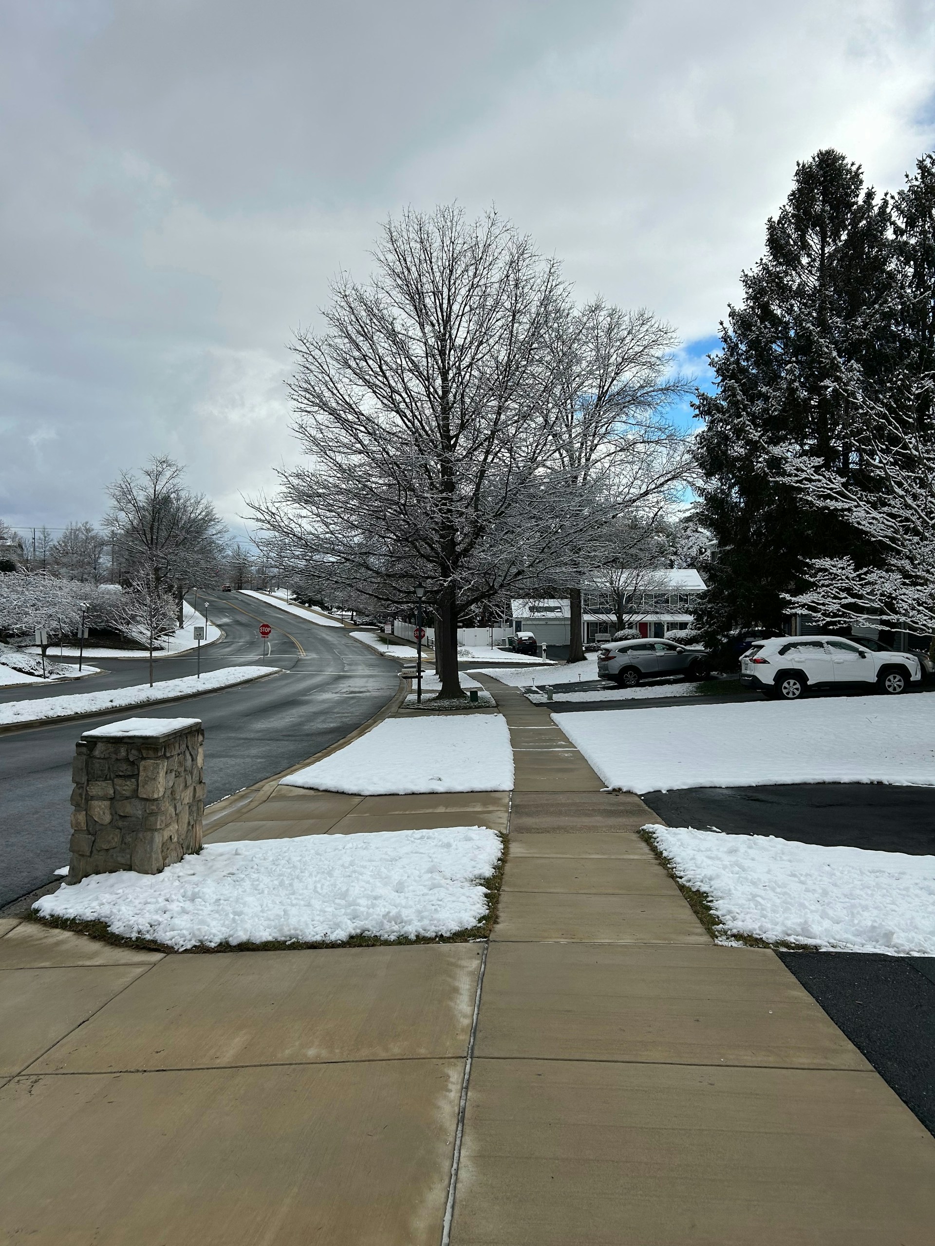 a sidewalk with snow on the ground and cars parked on the side of the road