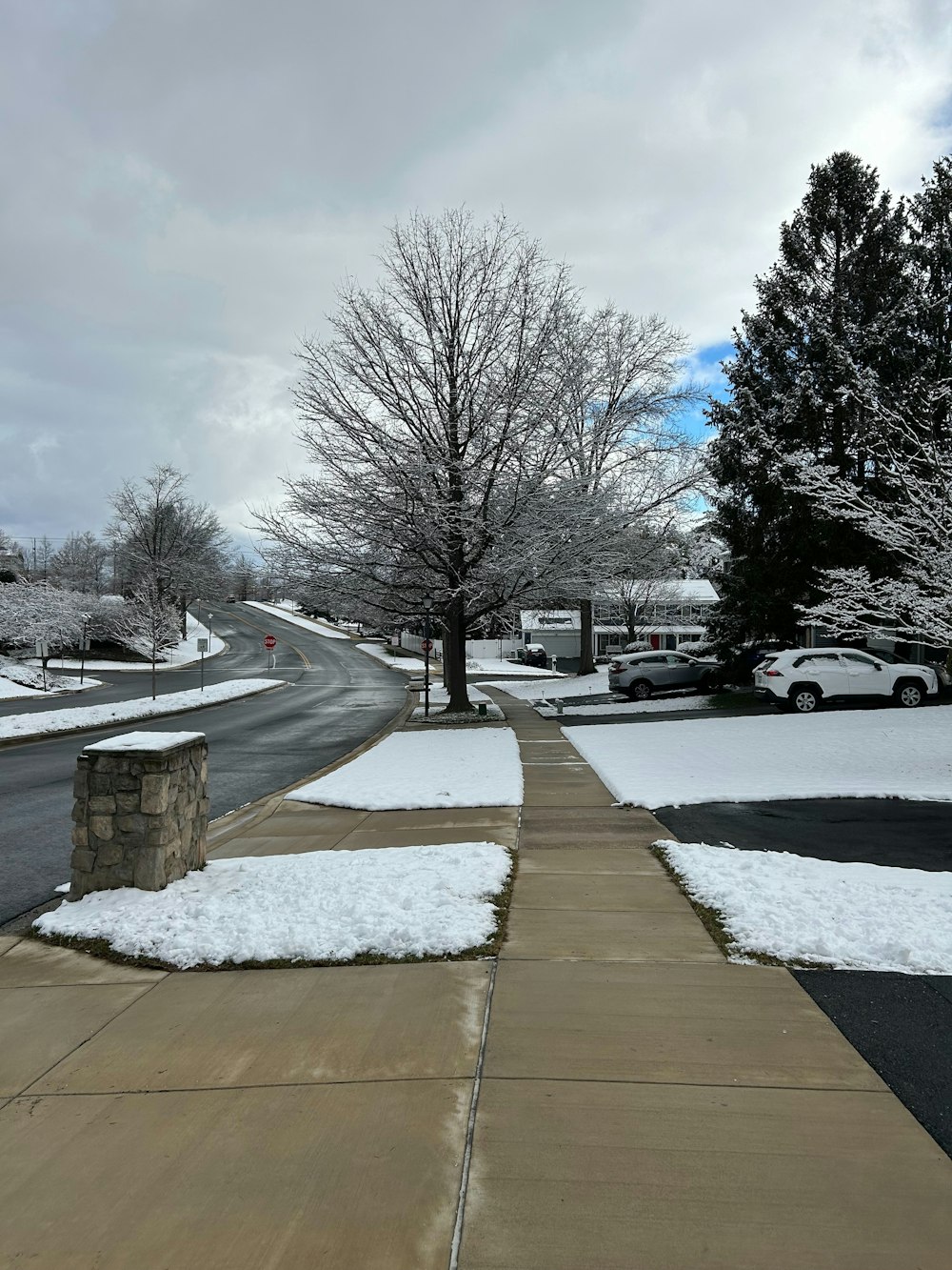 a sidewalk with snow on the ground and cars parked on the side of the road