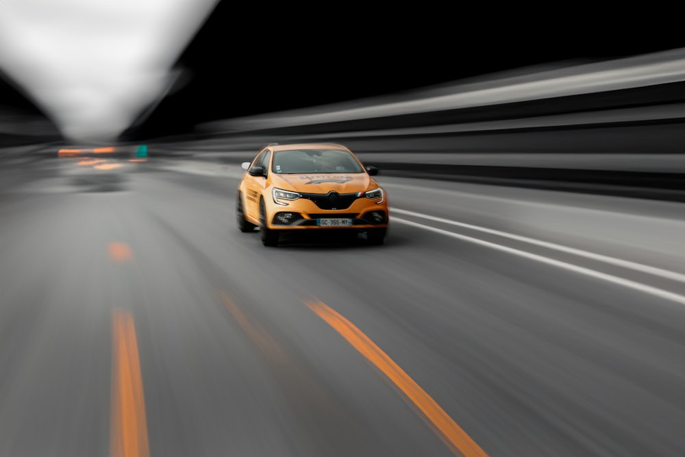 a yellow car driving down a street at night