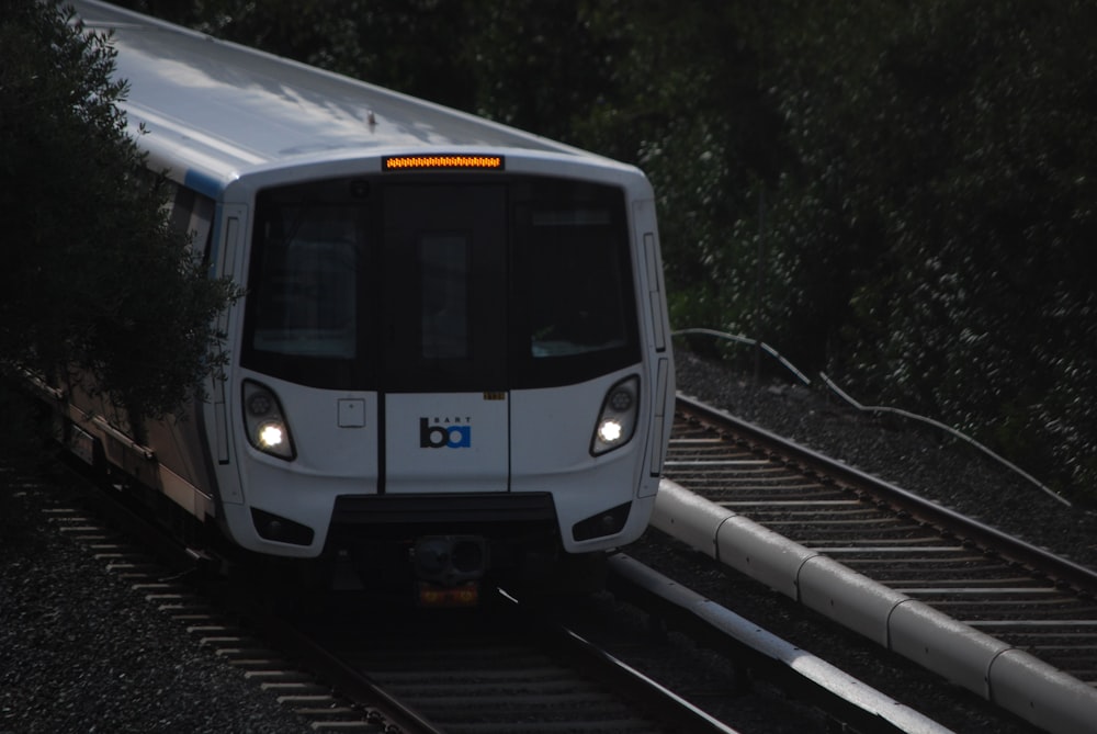 a white train traveling down train tracks next to a forest