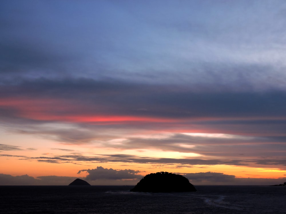 a sunset over a body of water with a small island in the distance