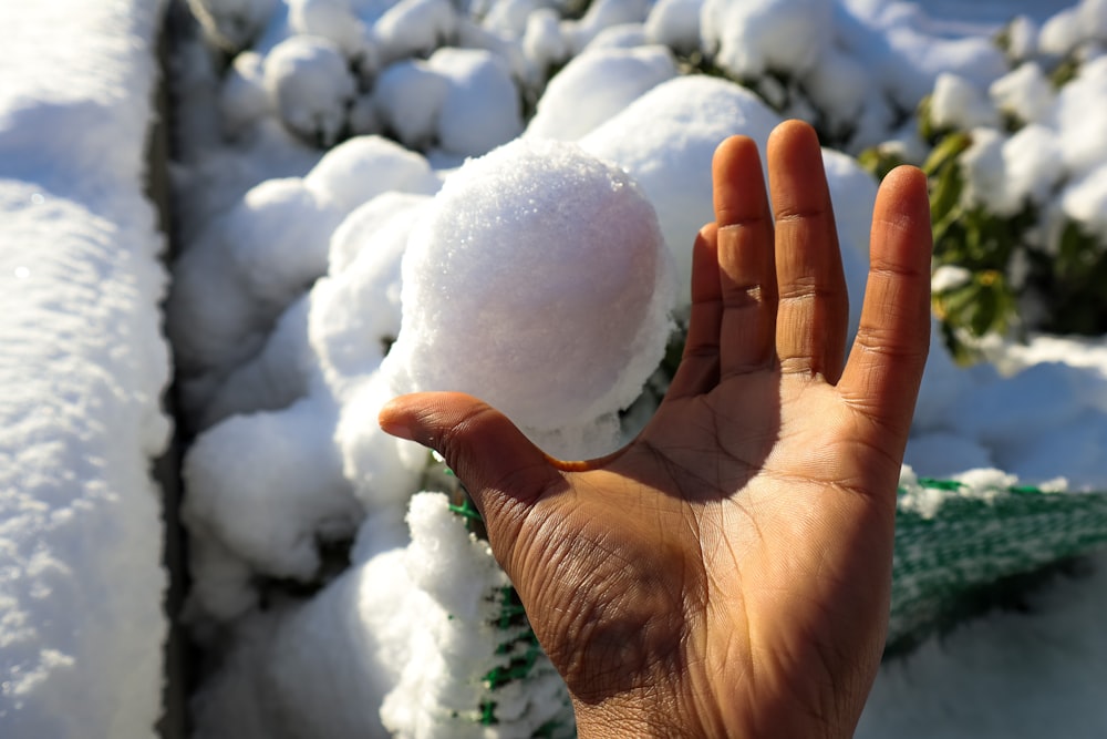 a hand holding a snowball in front of a pile of snow