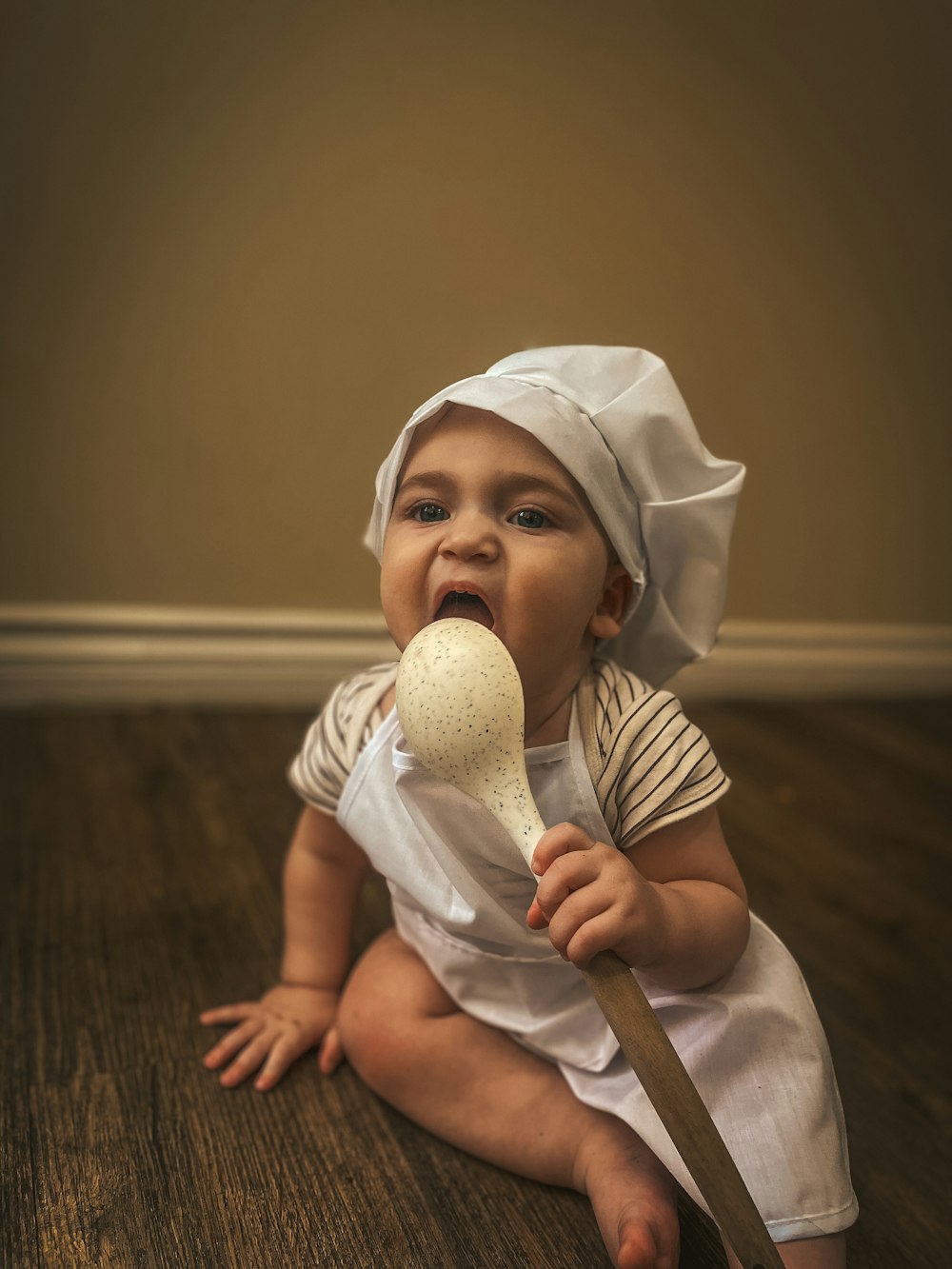 a baby sitting on the floor holding a wooden spoon