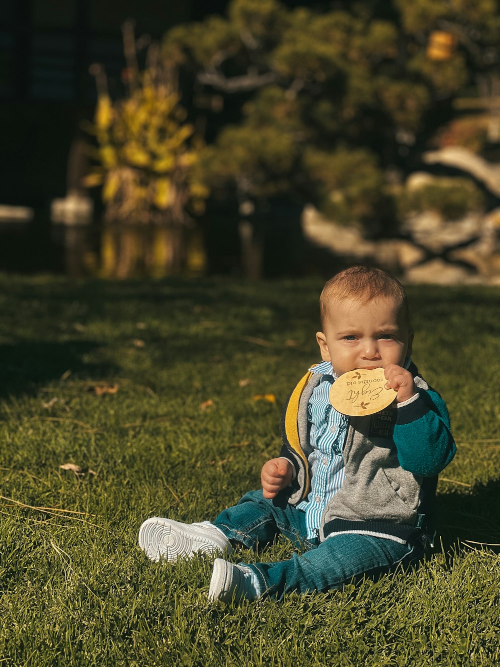 a baby sitting in the grass with a medal in his mouth