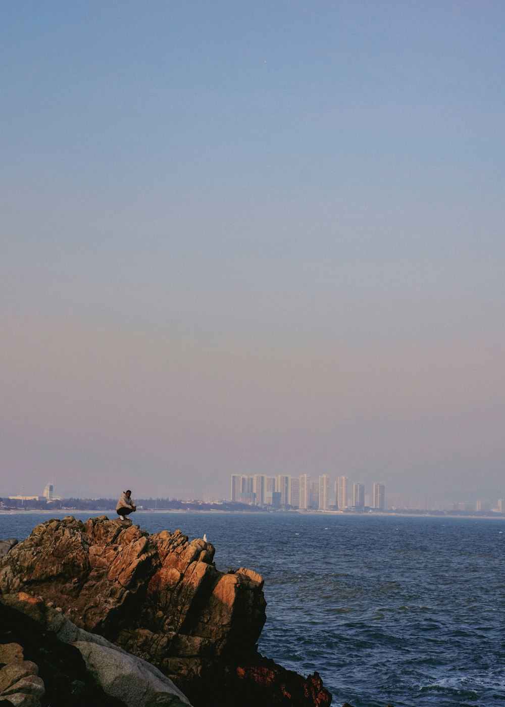 a person sitting on a rock near the ocean