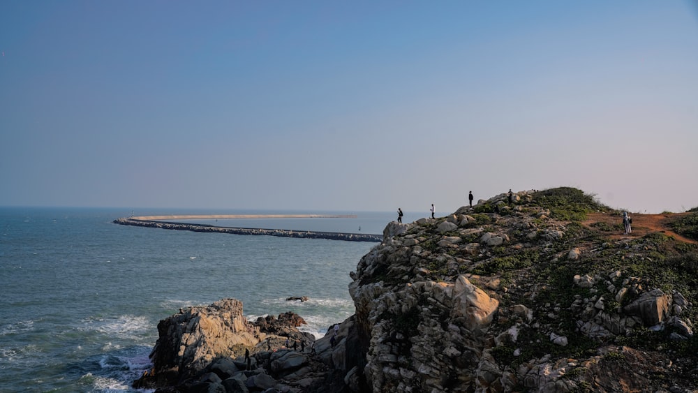 a group of people standing on top of a cliff next to the ocean