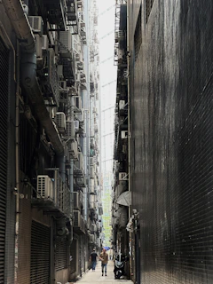 a couple of people walking down a street next to tall buildings