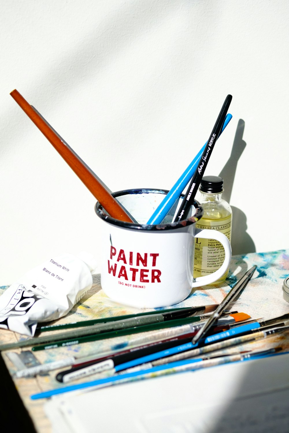 a cup with paint brushes and paints on a table