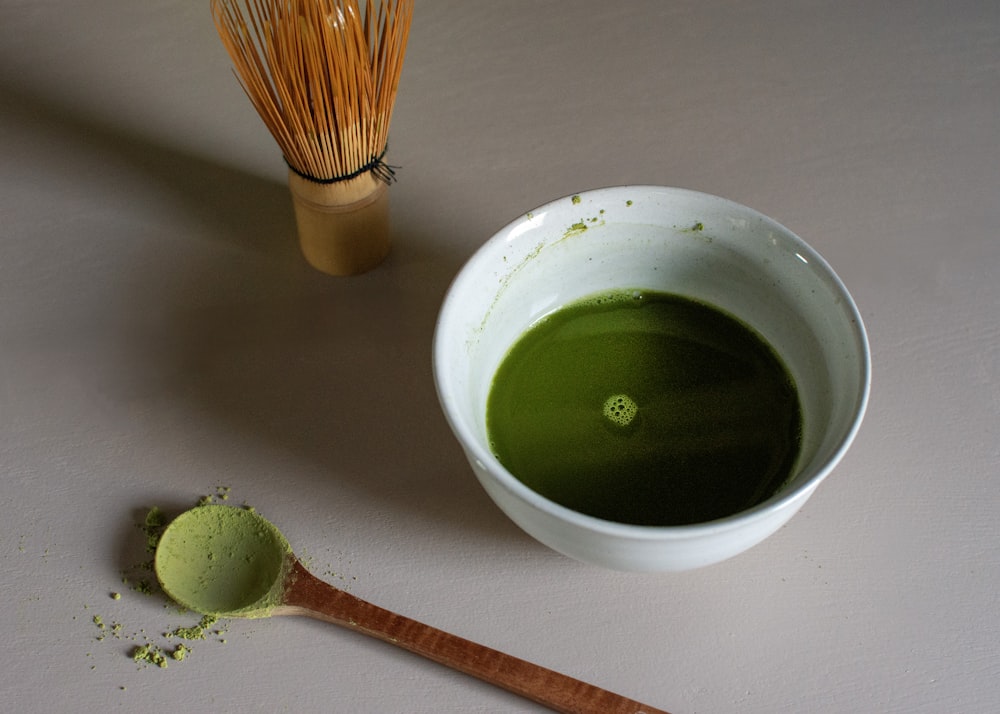 a bowl of green liquid next to a whisk