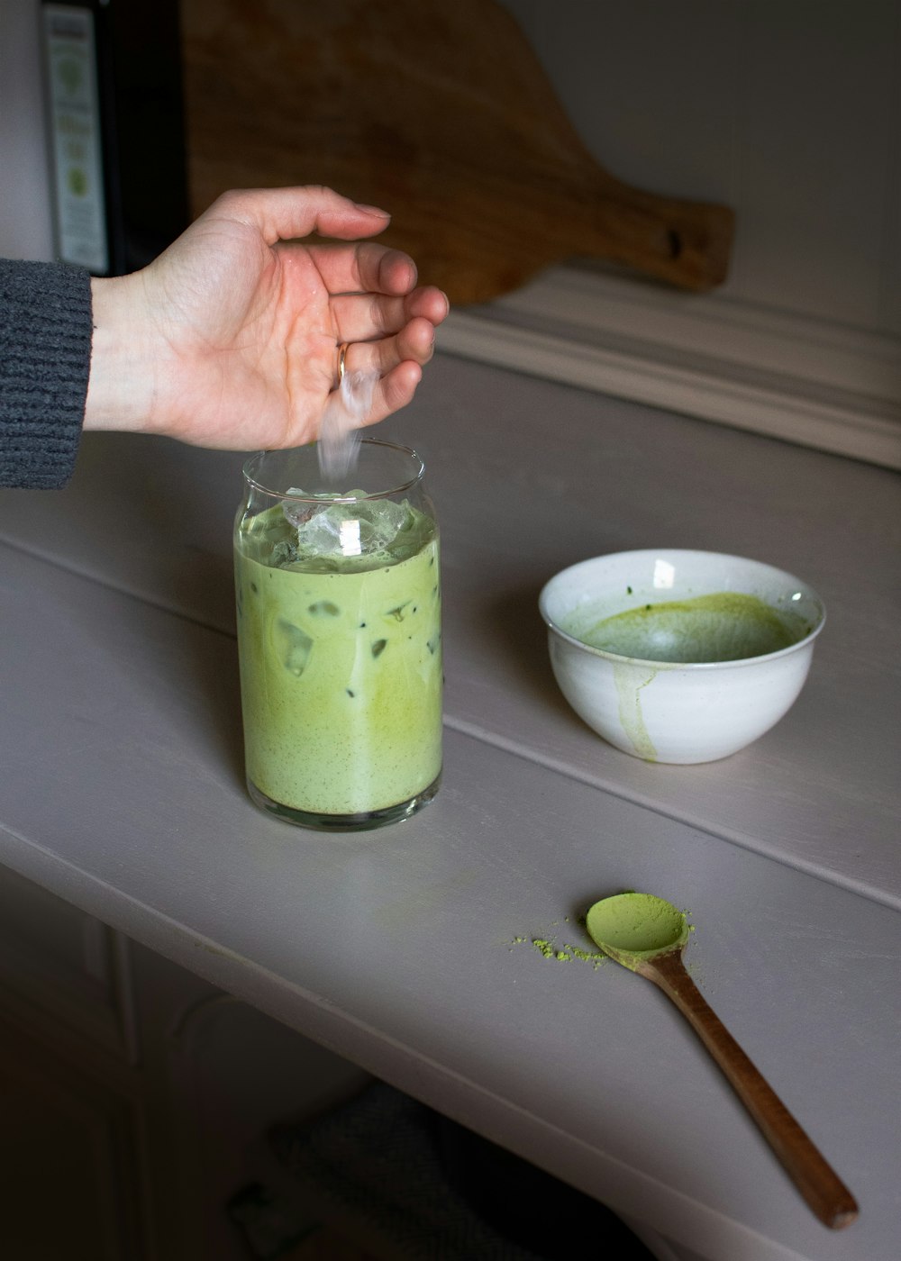 a person holding their hand over a cup of green liquid