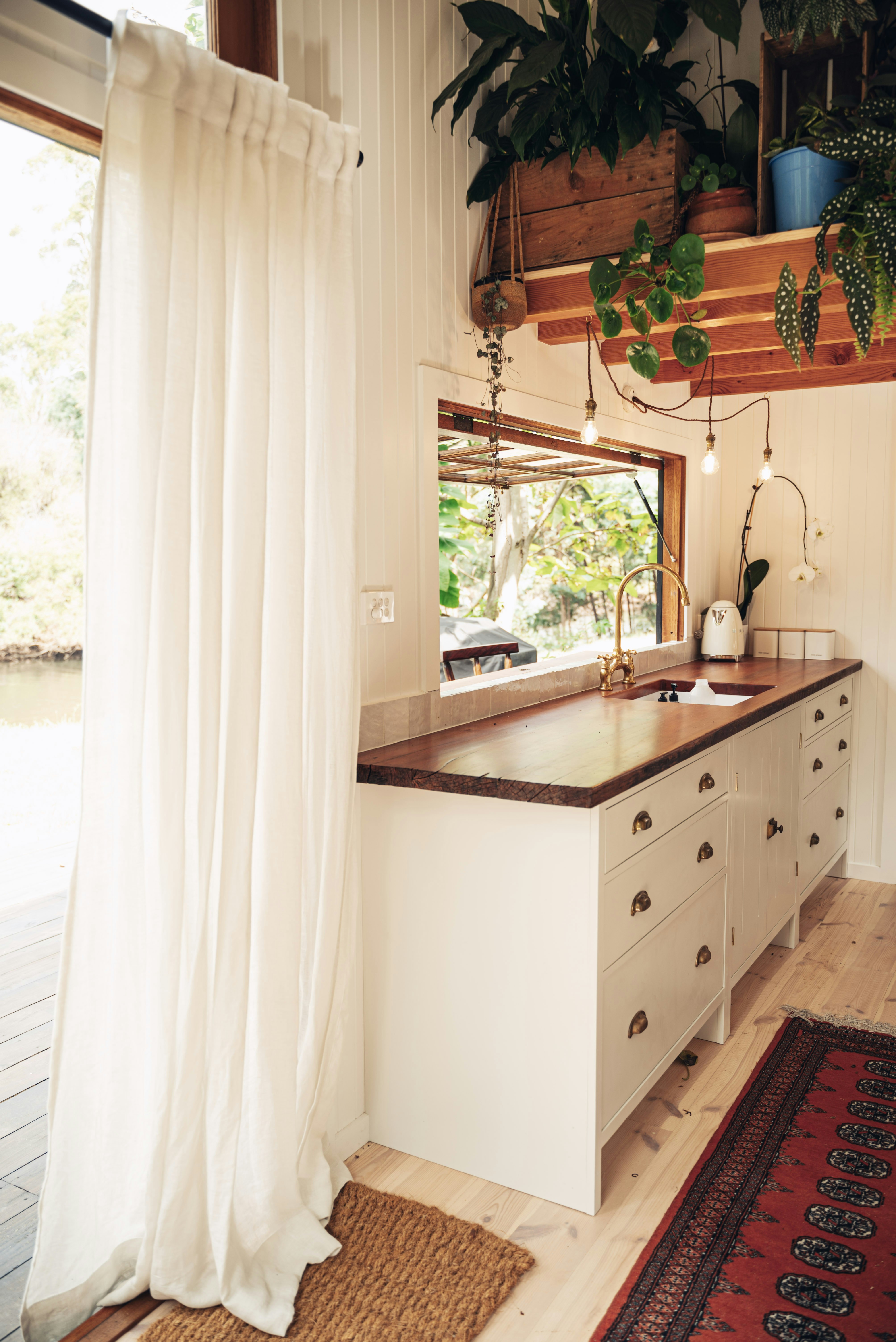 Minimalist kitchen with brass fixtures, white oak cabinetry, stone countertops, deep forest view, warm lighting