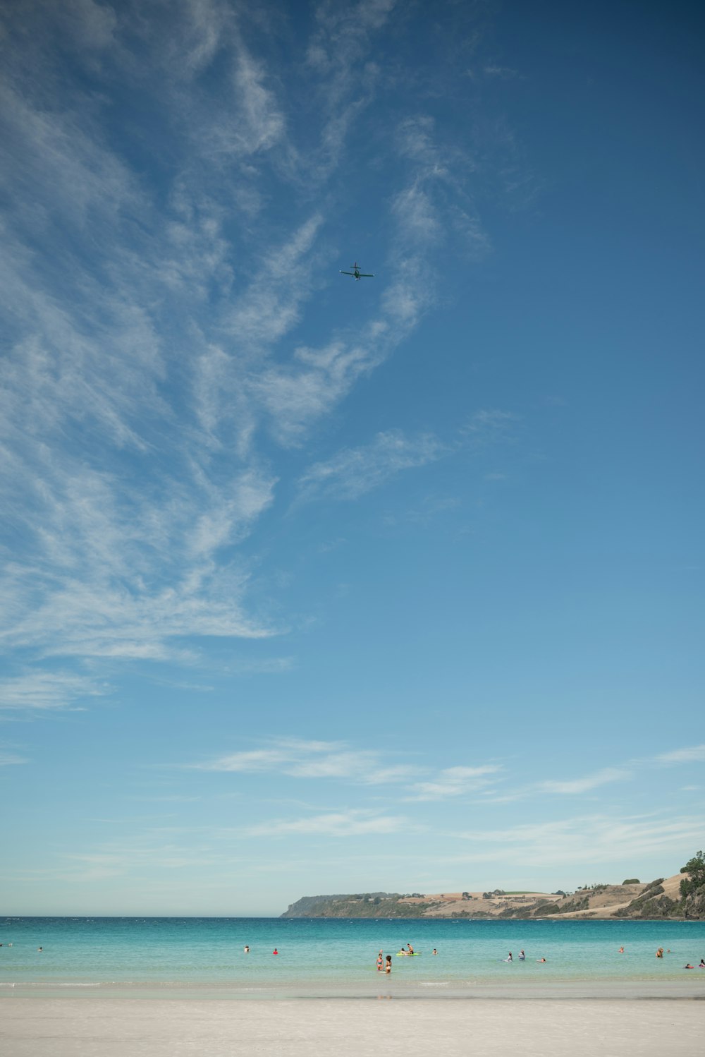 a plane flying over a beach with people in the water