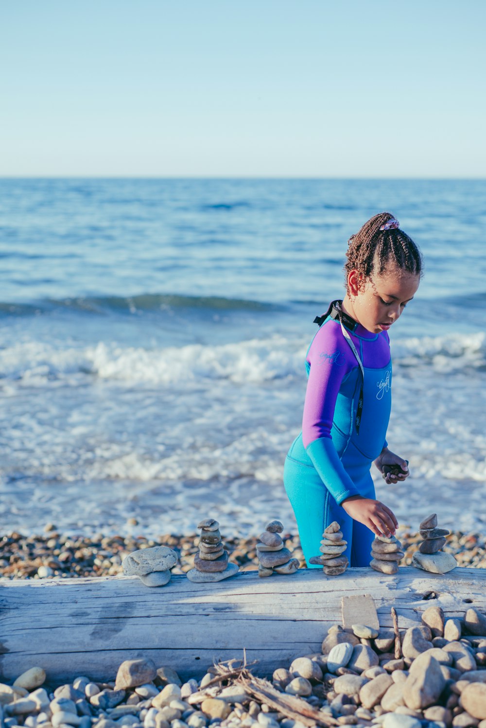 a little girl in a wetsuit playing with rocks on the beach