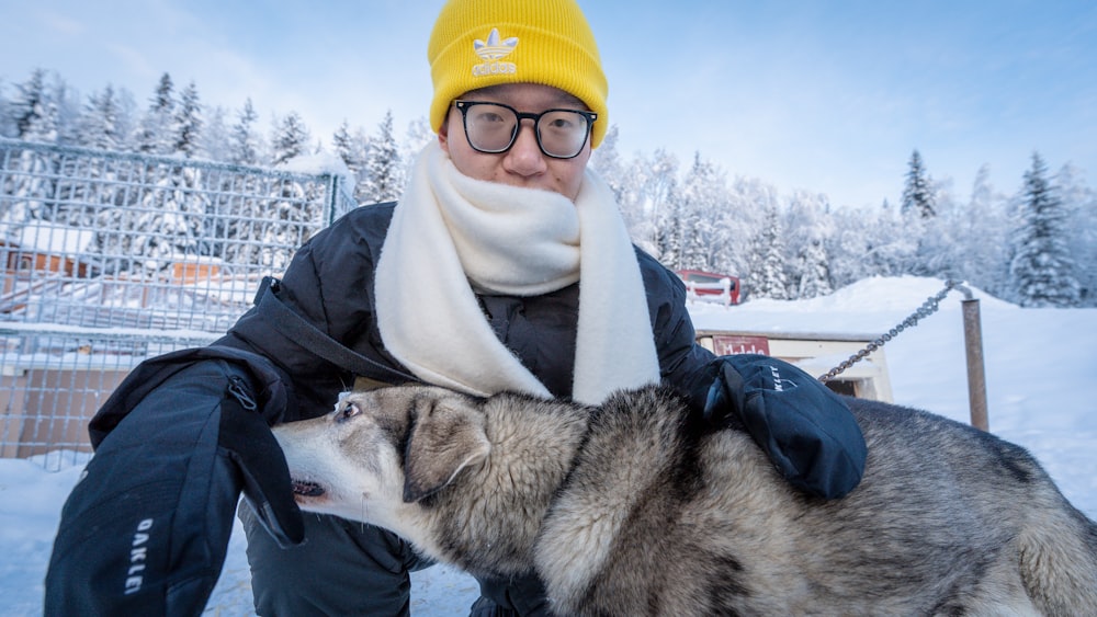 a man kneeling down next to a dog in the snow